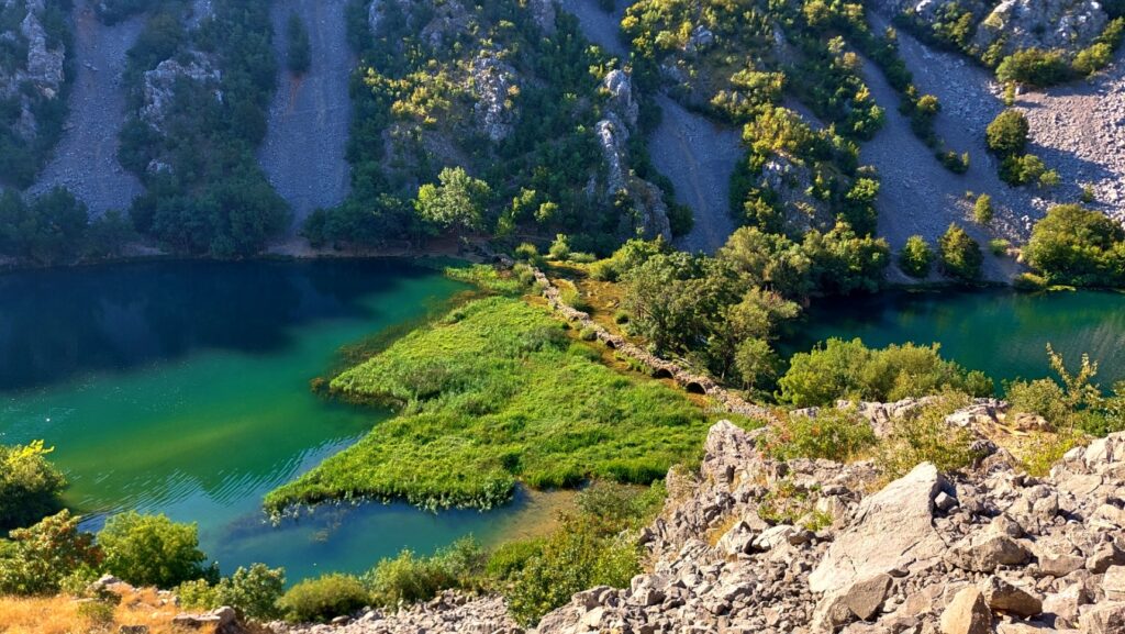 Kudin Most visto dall’alto, con il ponte di travertino immerso tra acqua turchese e vegetazione lungo il sentiero di discesa.