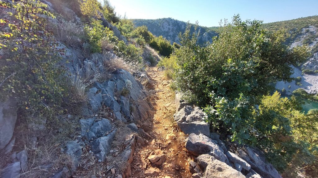 Sentiero roccioso in discesa tra vegetazione e pietra, lungo il percorso per raggiungere Kudin Most.