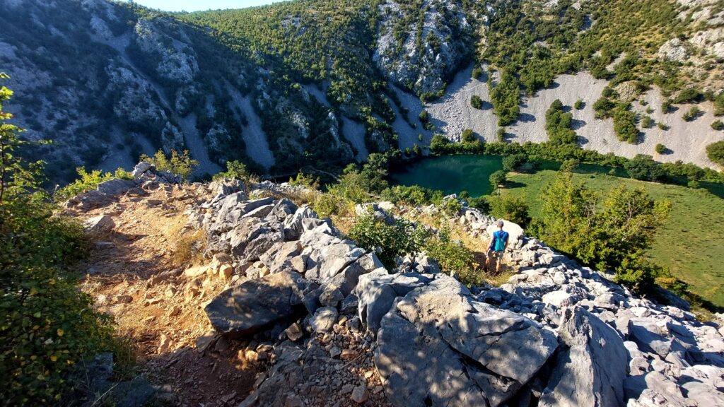 Sentiero roccioso un po' sconnesso in discesa a tornanti tra vegetazione e pietra, lungo il percorso per raggiungere Kudin Most.