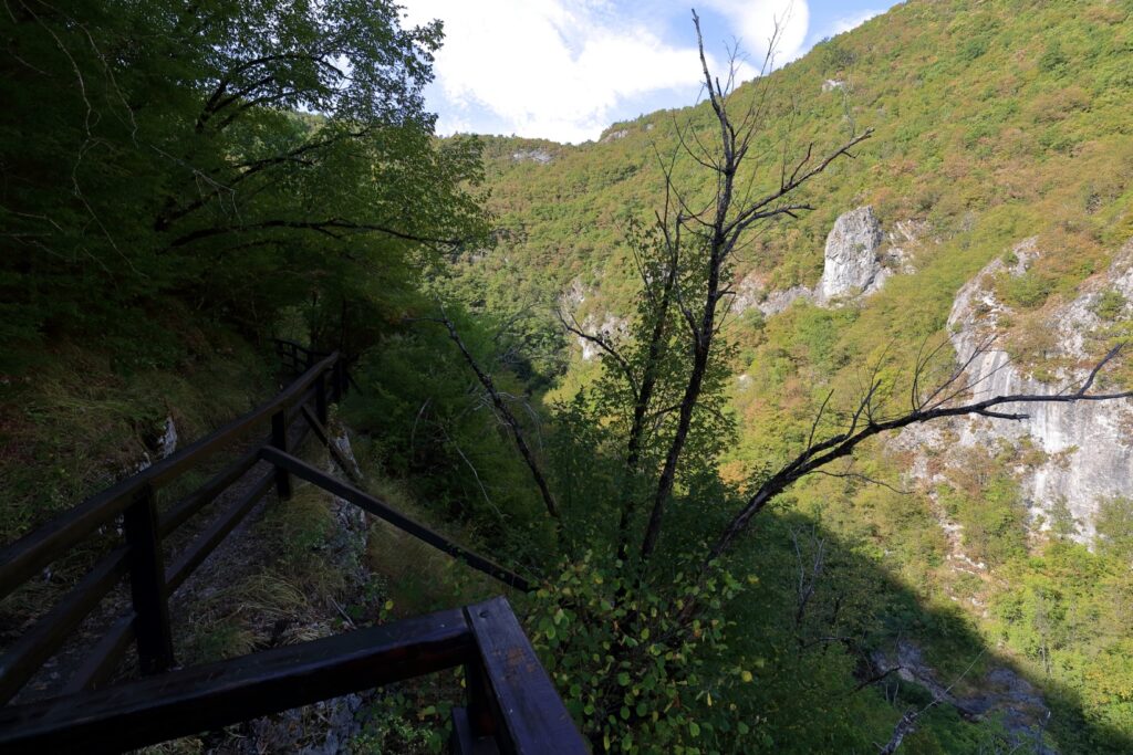 Punto panoramico lungo il sentiero per la sorgente dell’Una, con corrimano in legno e vista parziale sulla valle tra vegetazione e pareti rocciose.